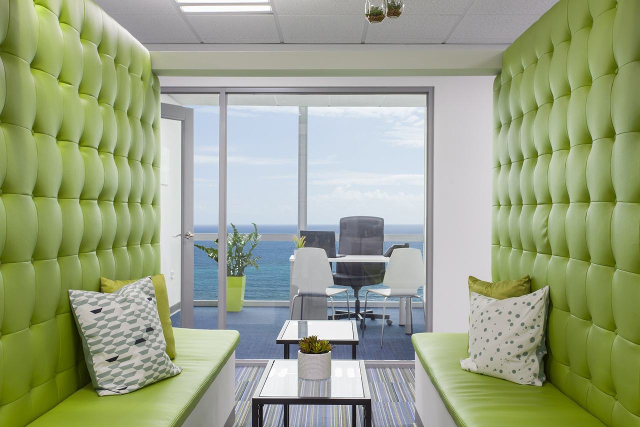 Lounge with lime-green tufted booths looking through a glass office to the ocean